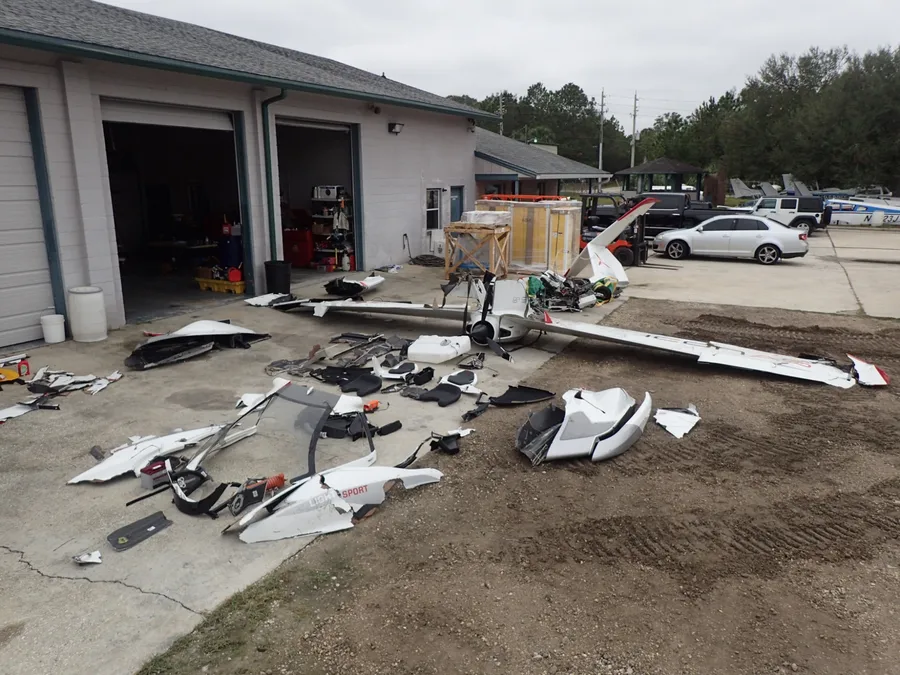 Recovered wreckage laid out for examination at a recovery yard, fuselage and wings separated into sections