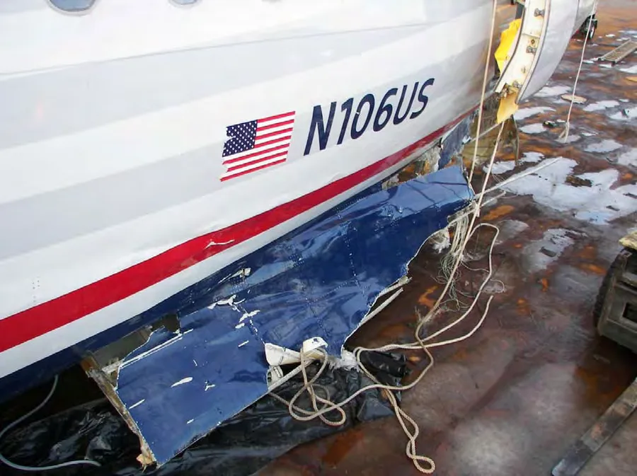 Close-up of the lower forward fuselage of N106US showing torn skin and impact damage near the registration marking